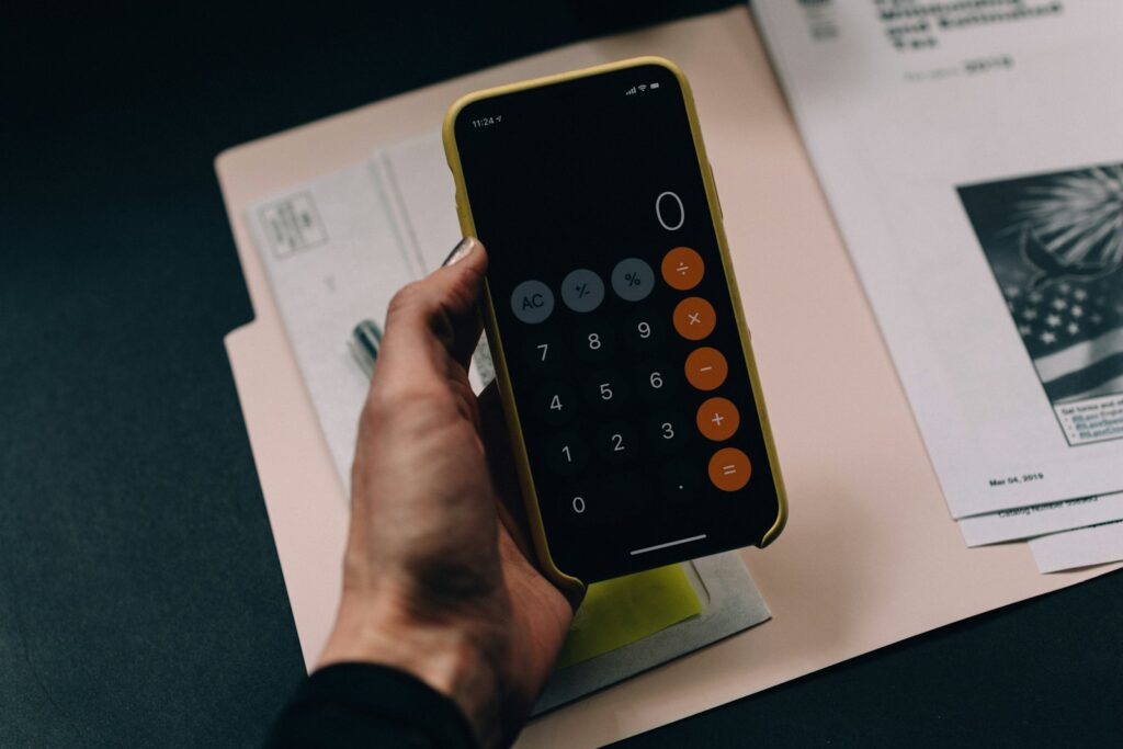 Mano sosteniendo un celular con calculadora sobre una carpeta de papeles