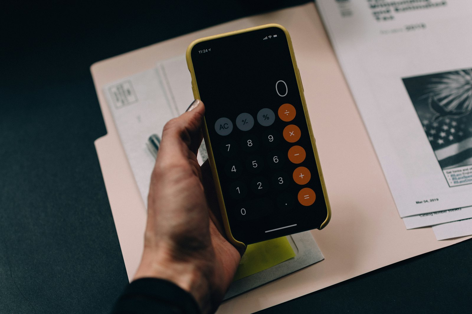 Mano sosteniendo un celular con calculadora sobre una carpeta de papeles